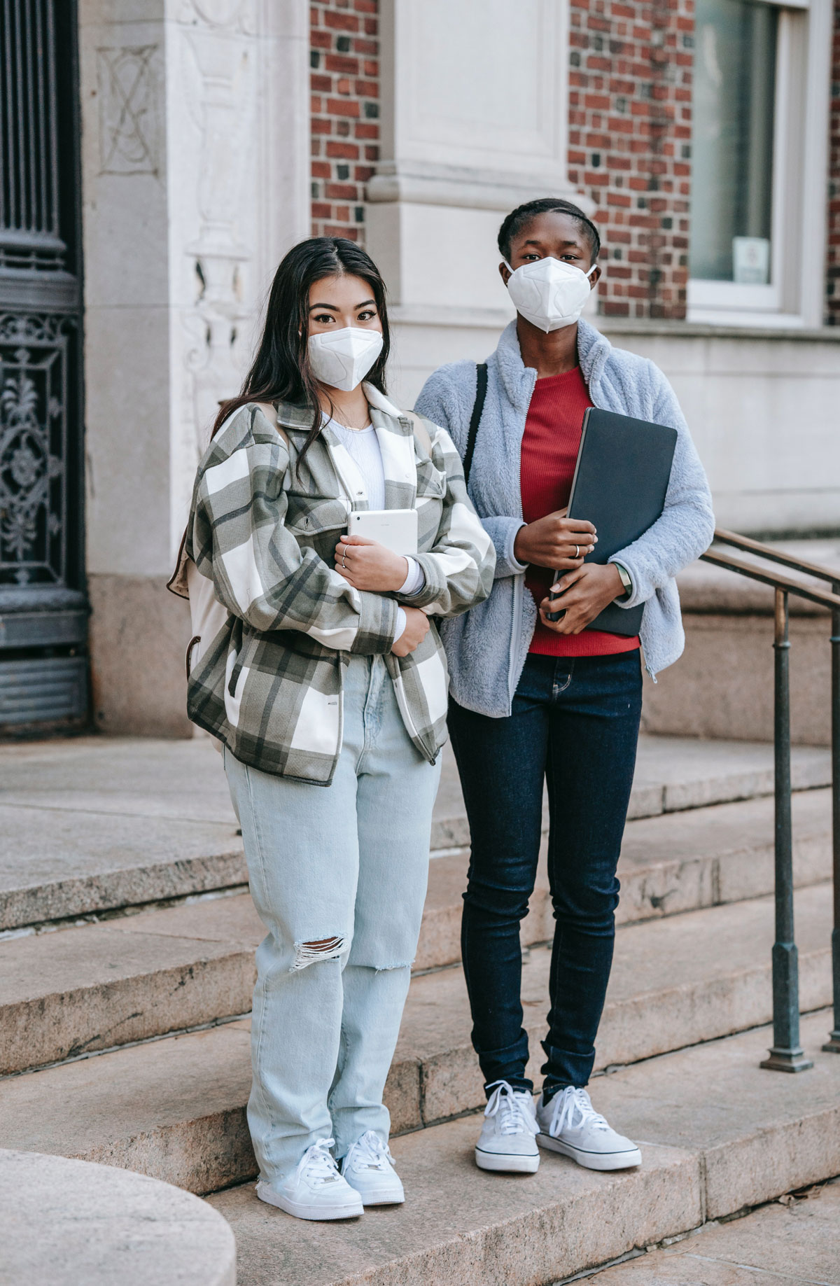 Two students stand on the steps at the entrance to school wearing masks
