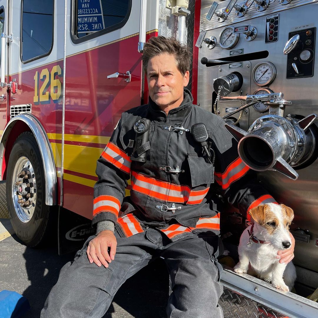 Rob Lowe dressed as a firefighter and sitting on a firetruck with his dog, via Instagram