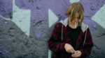 Teen boy smoking up against a wall, his head is down