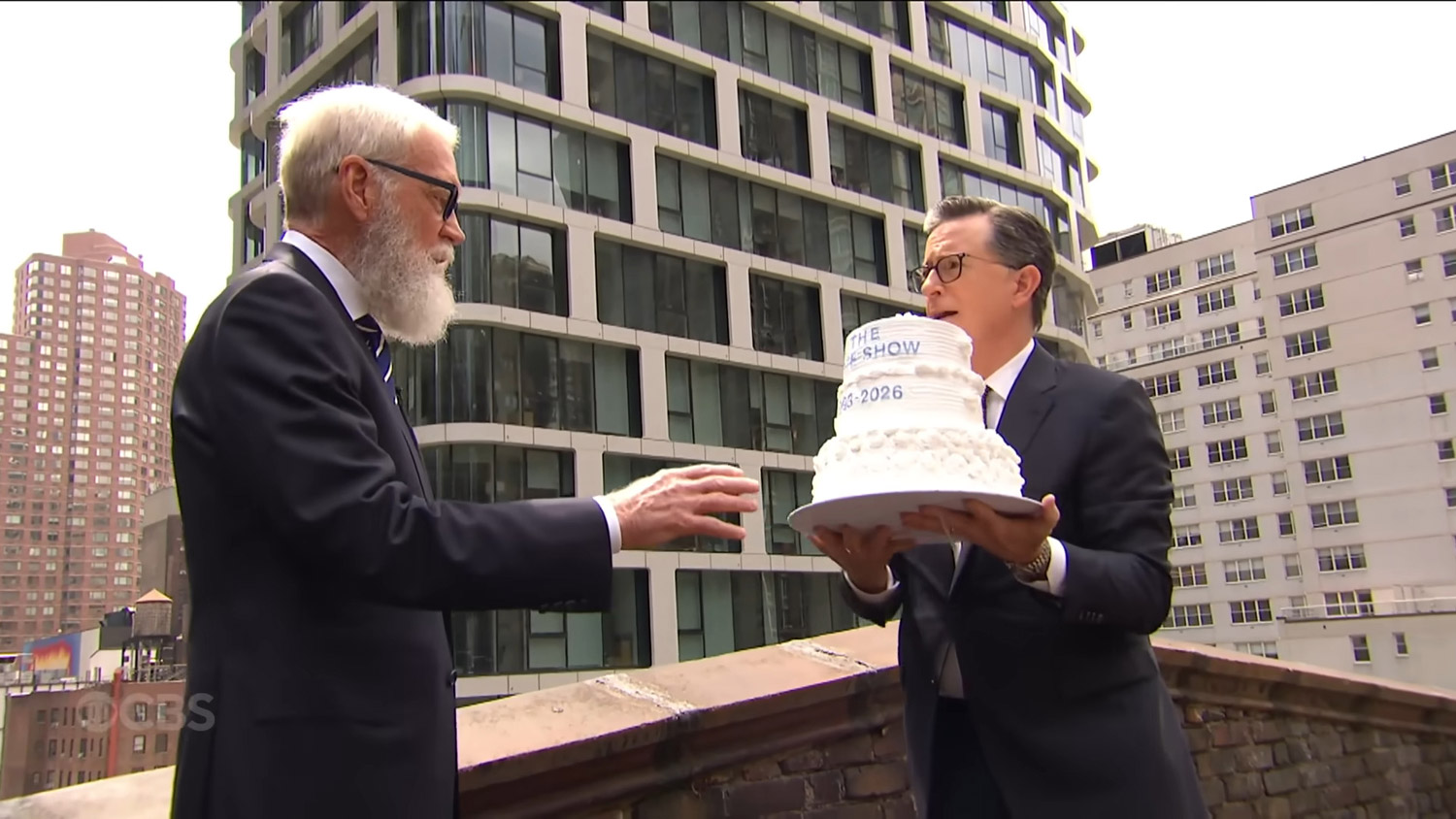 Colbert holding a cake next to Letterman. They're about to throw it off the roof