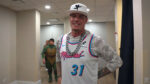 Vanilla Ice wearing a camo shirt and tank top over it, large change and a hat with a sillouhette of a cupid holding an AK