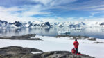 Couple standing on a rock formation and wearing orange jackets looking out into the ocean in Antarctica