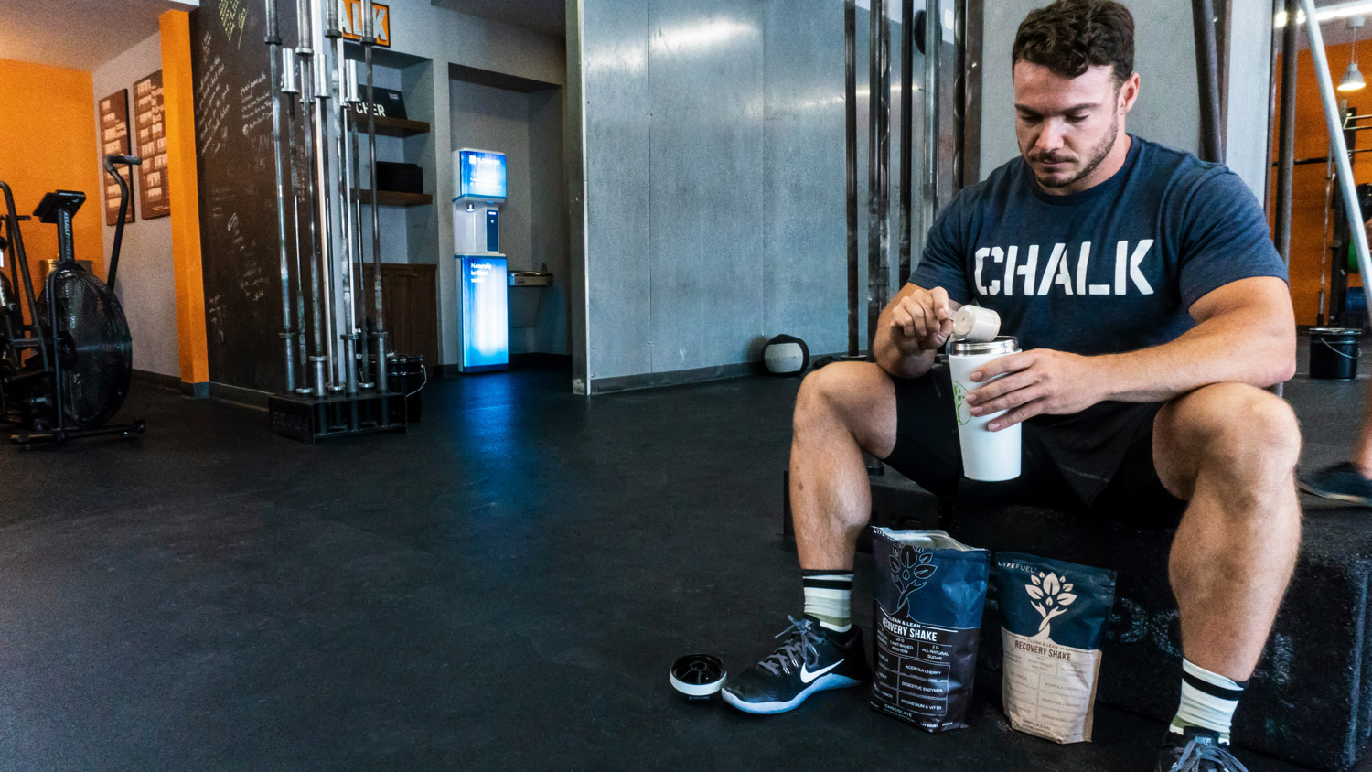man in a gym sitting down drinking a protein shake
