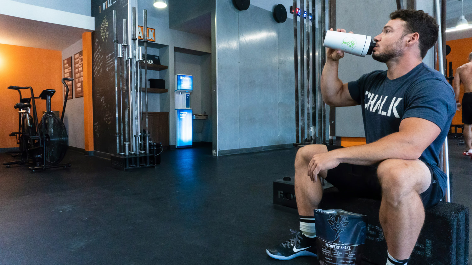 man in a gym sitting down drinking a protein shake