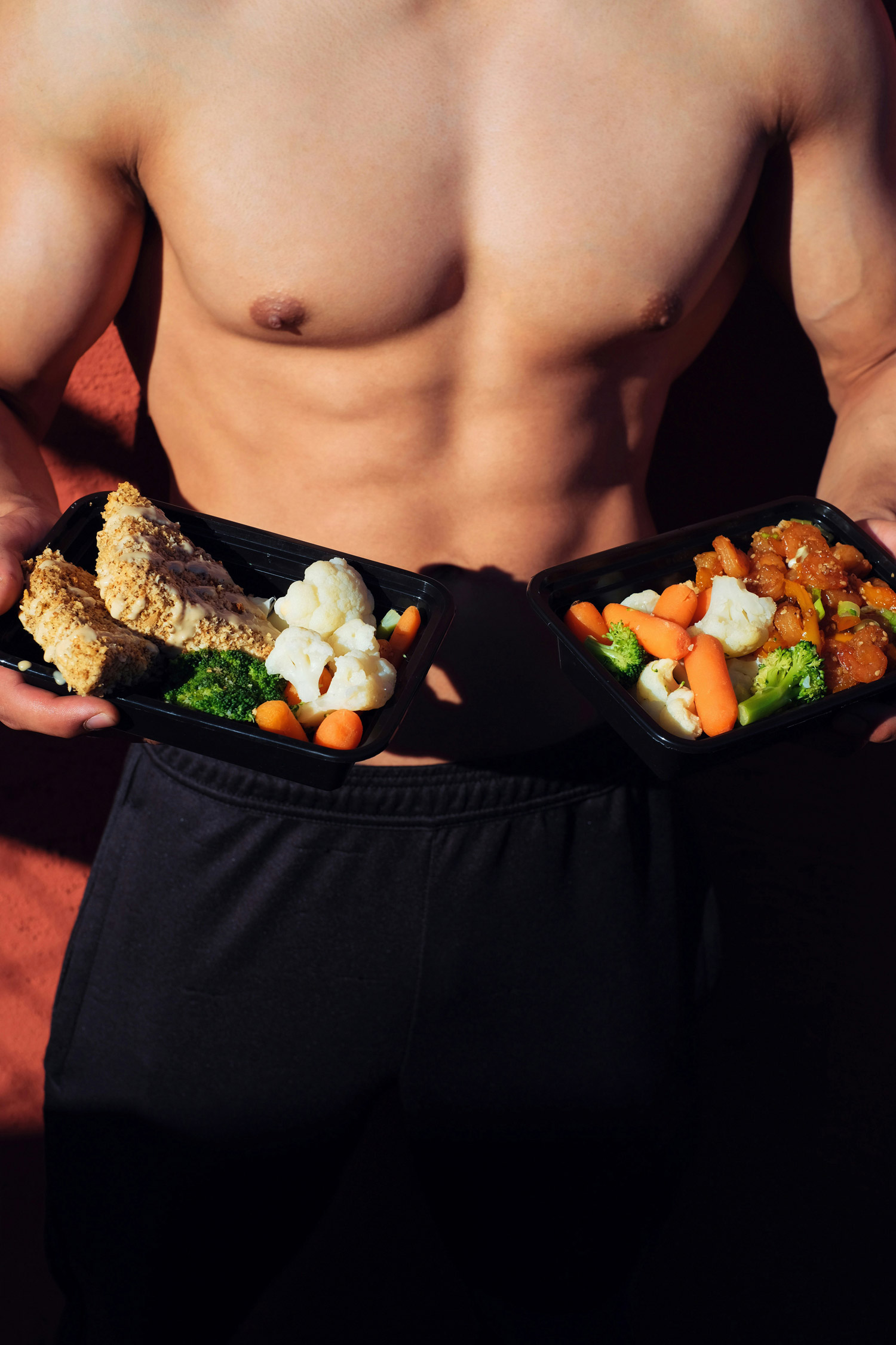bare toned male stomach with a takeaway container of healthy food
