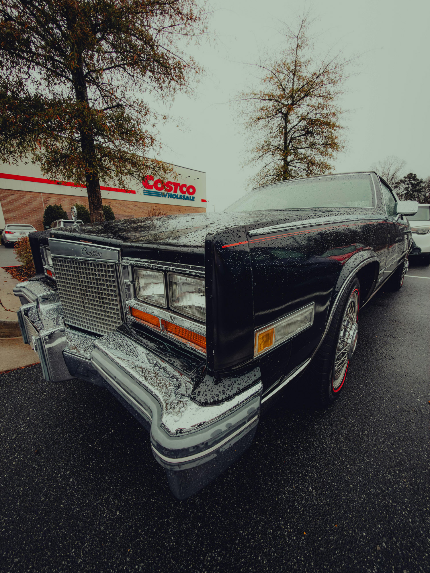 vintage car parked outside a Costco in a rainy setting