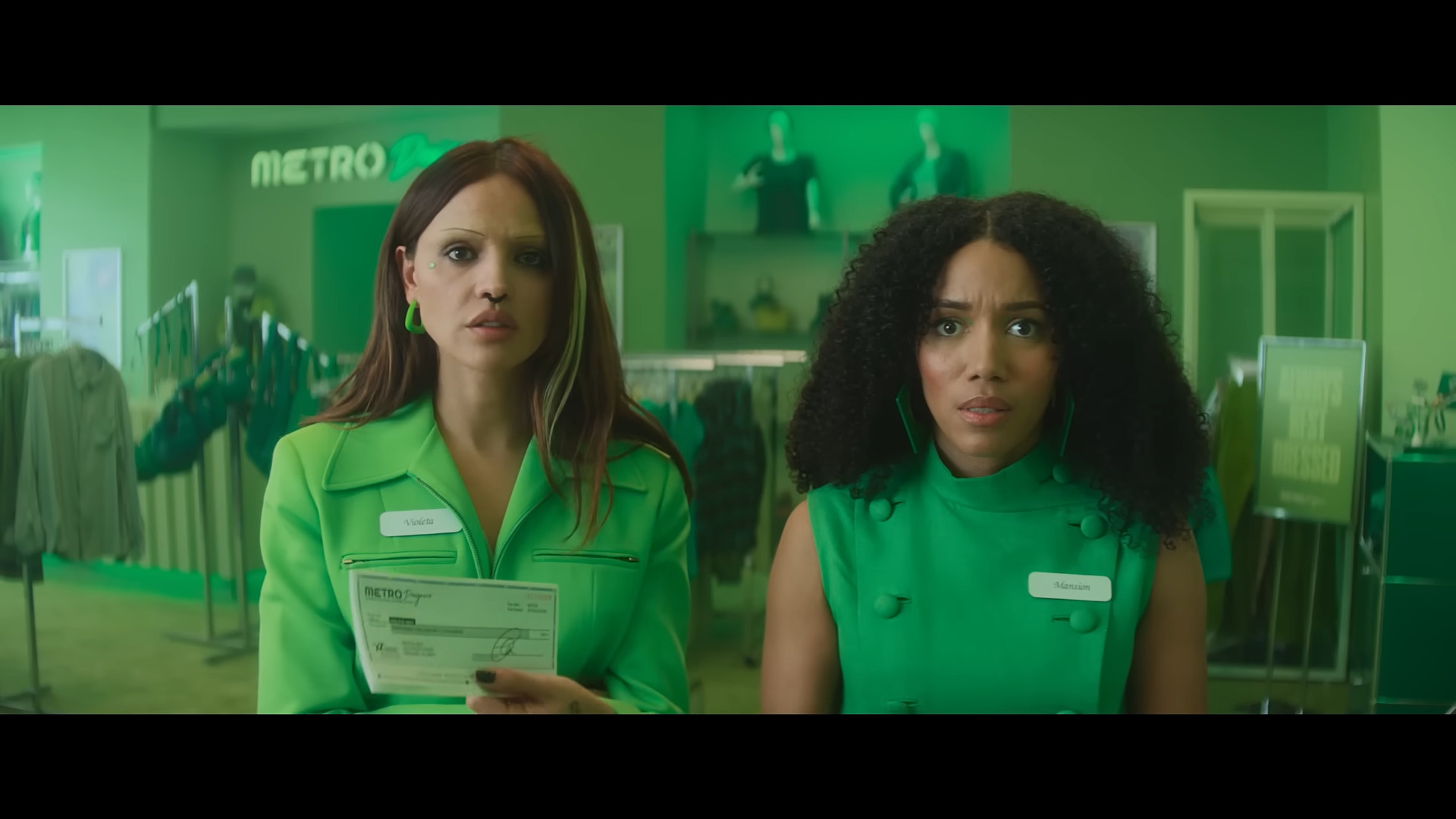 Eiza González and Najah Bradley all in green with green clothing in the background in I Love Boosters