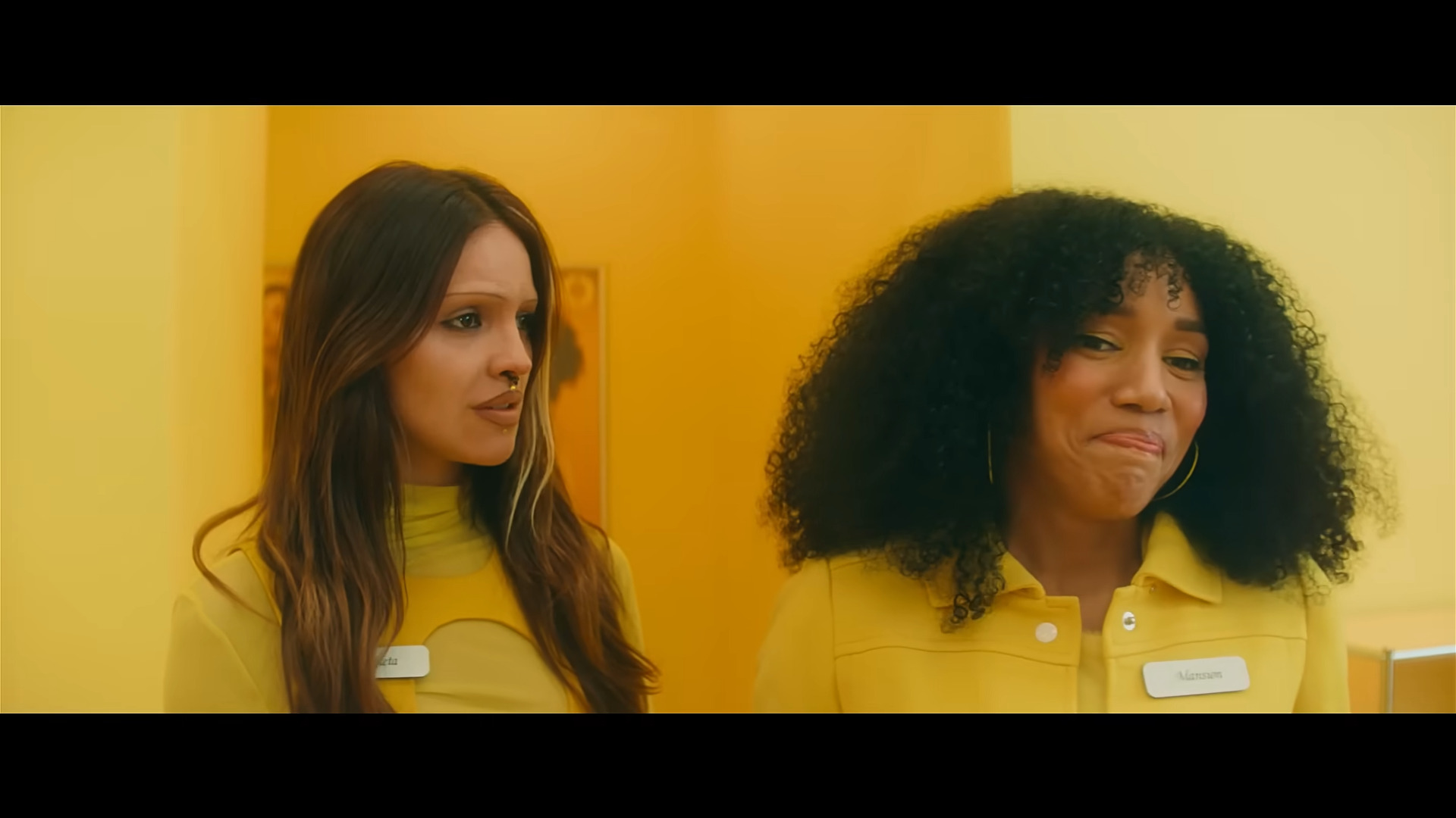 Eiza González and Najah Bradley cracking up all in orange with an orange background in I Love Boosters