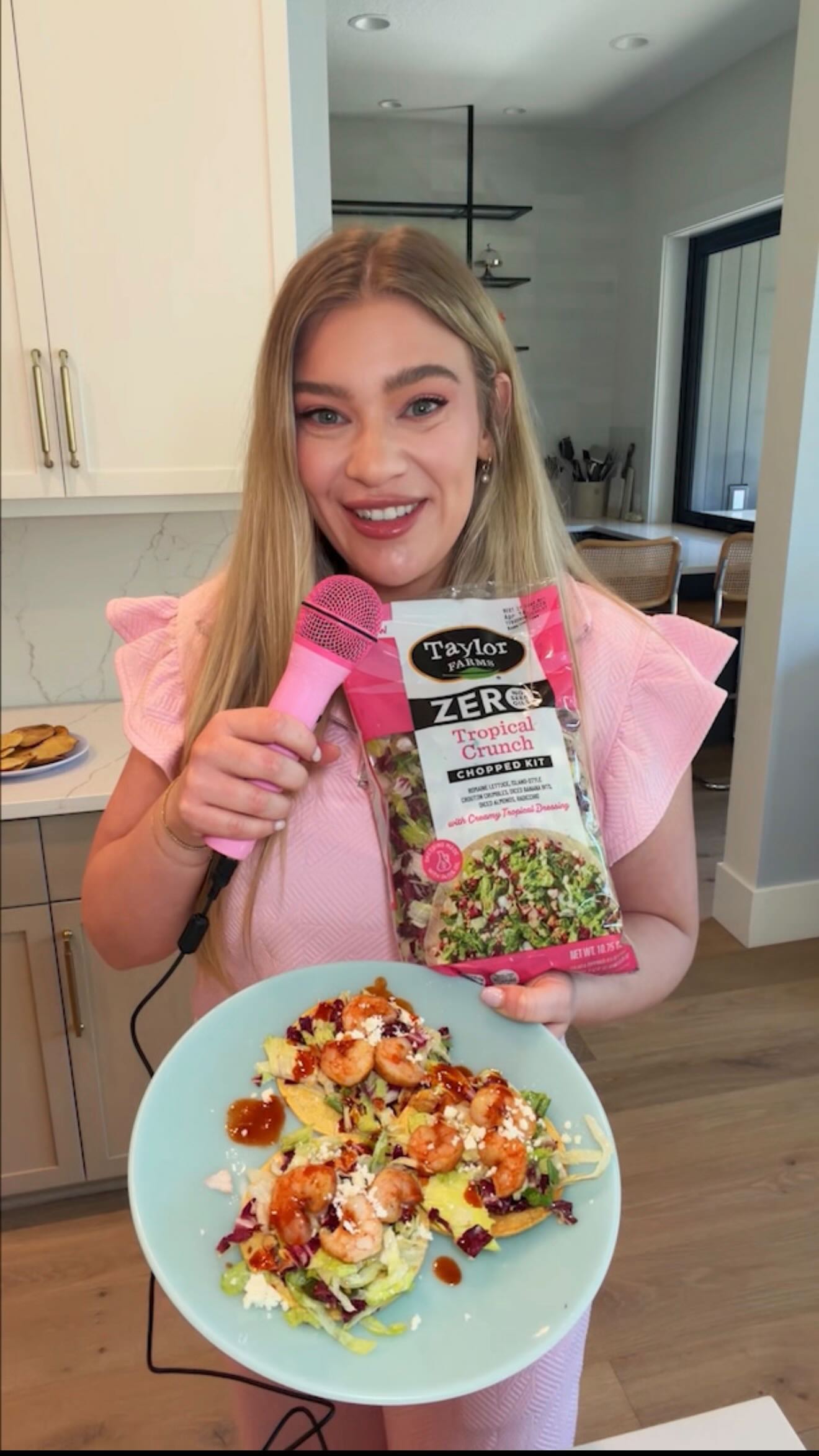 Woman holding a pink microphone and a Taylor Farms salad kit
