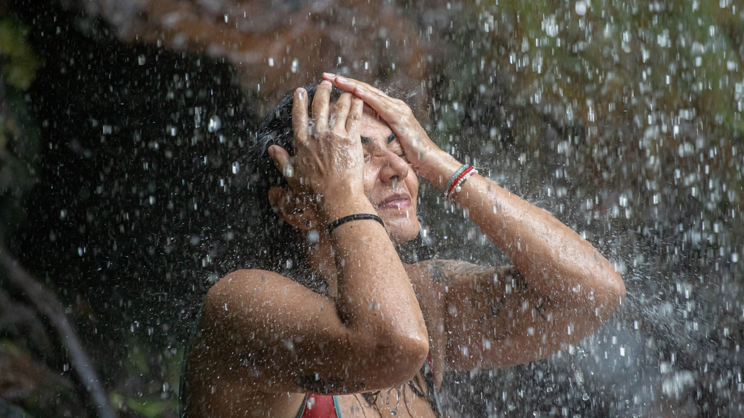 Woman showering and putting hands up to her face, she is wearing a bikini