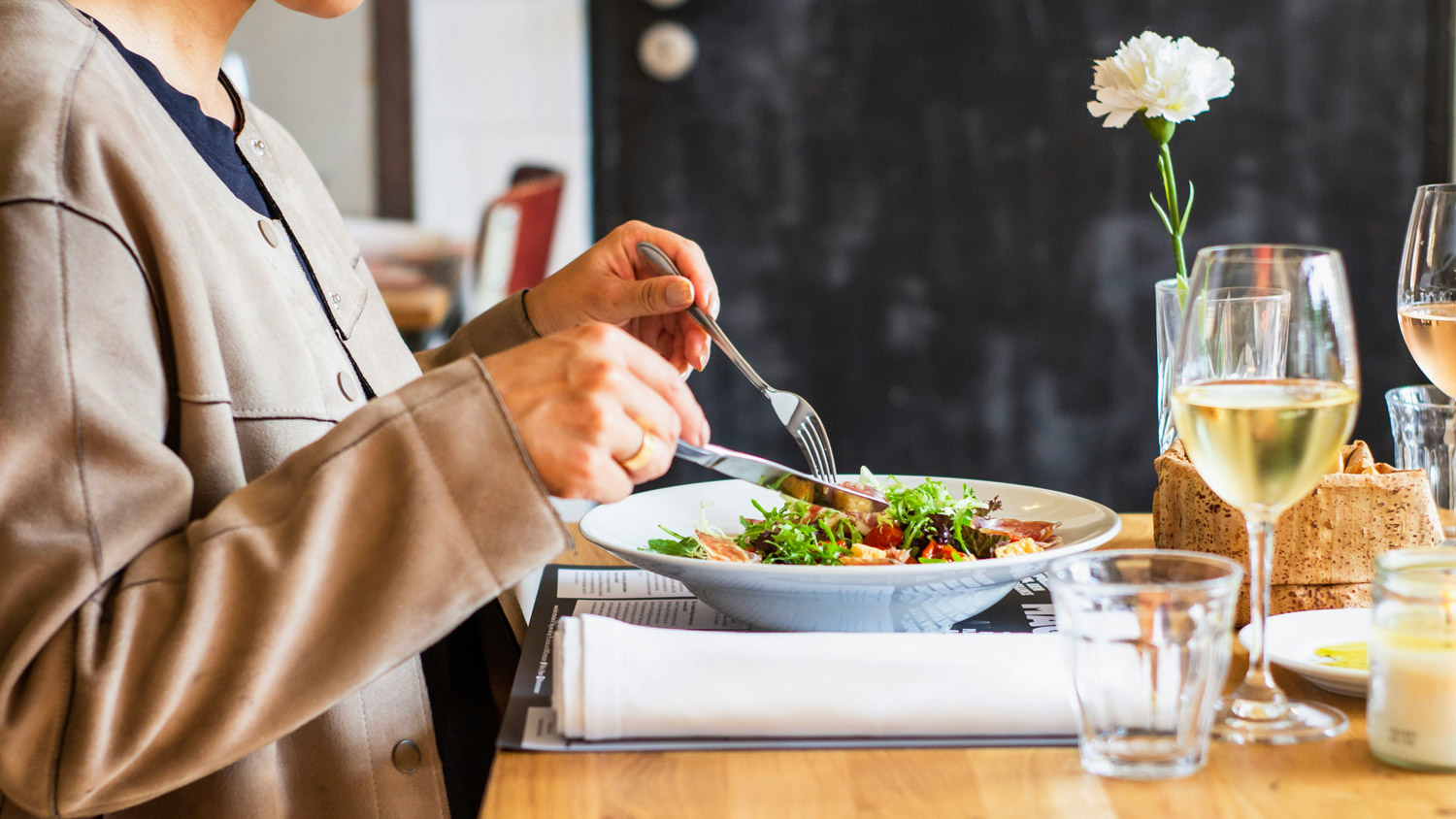 view of a person's hands and torso as they eat salad at a restaurant