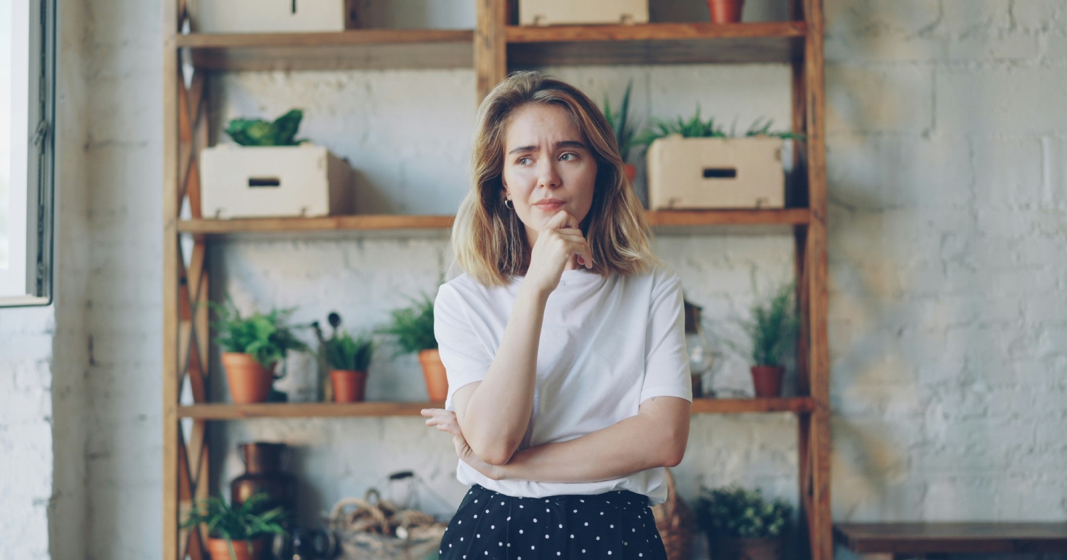 Woman with a furrowed brow while standing in front of a shelf with plants