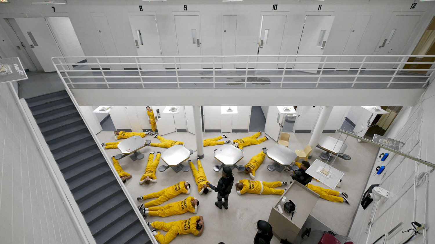 above view of prisoners on ground in prison common area with guards around