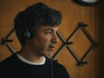 Nathan Fielder with headphones on looking concerned