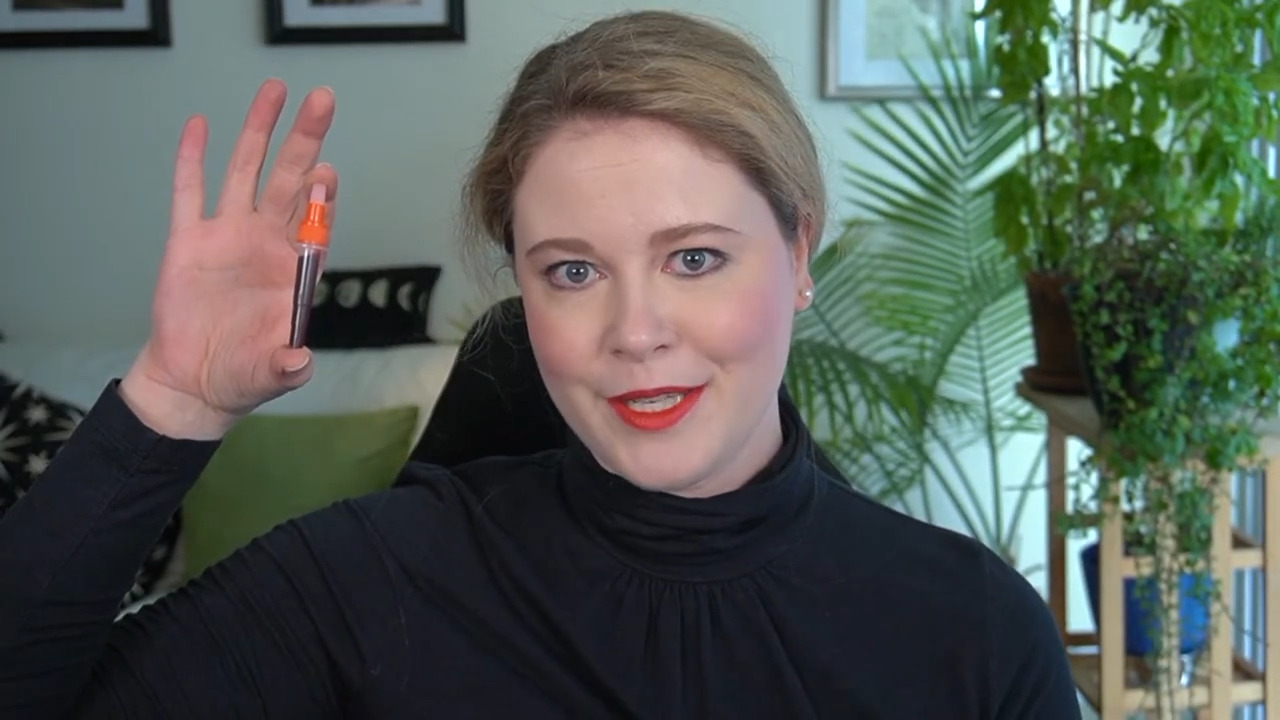 Woman holding up a vial wearing her hair back in a black turtleneck